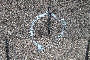 Chalk-drawn peace symbol on a hail damage-marked asphalt surface.