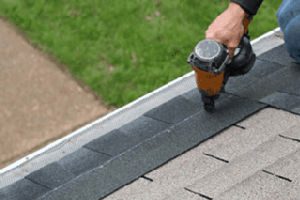 Worker using a nail gun on a shingled roof for roof replacement.