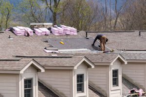 Worker installing or repairing shingles on a residential roof during the best season for roof replacement.