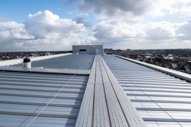 Industrial metal roofing installation on a commercial building with corrugated panels and ridge cap, overlooking San Antonio cityscape under cloudy sky