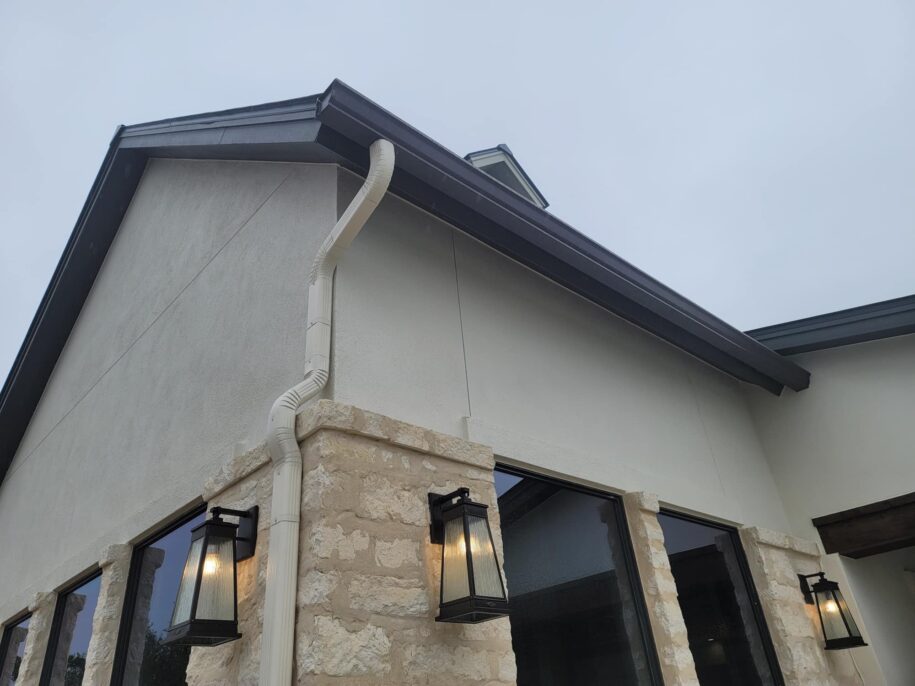 Modern home exterior featuring cream stone and white stucco with dark roof, black framed windows, and cream downspout gutter system in San Antonio