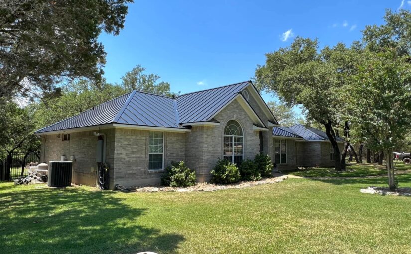 Modern brick home with dark metal pitched roof and seamless gutters surrounded by mature oak trees in San Antonio, Texas