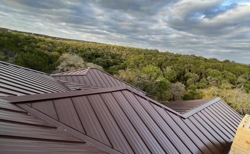 Modern metal roof installation with multiple peaks overlooking Texas hill country landscape with dense green forest canopy