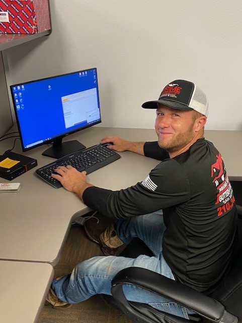 Man in roofing company cap and shirt sitting at desk working on computer in San Antonio office