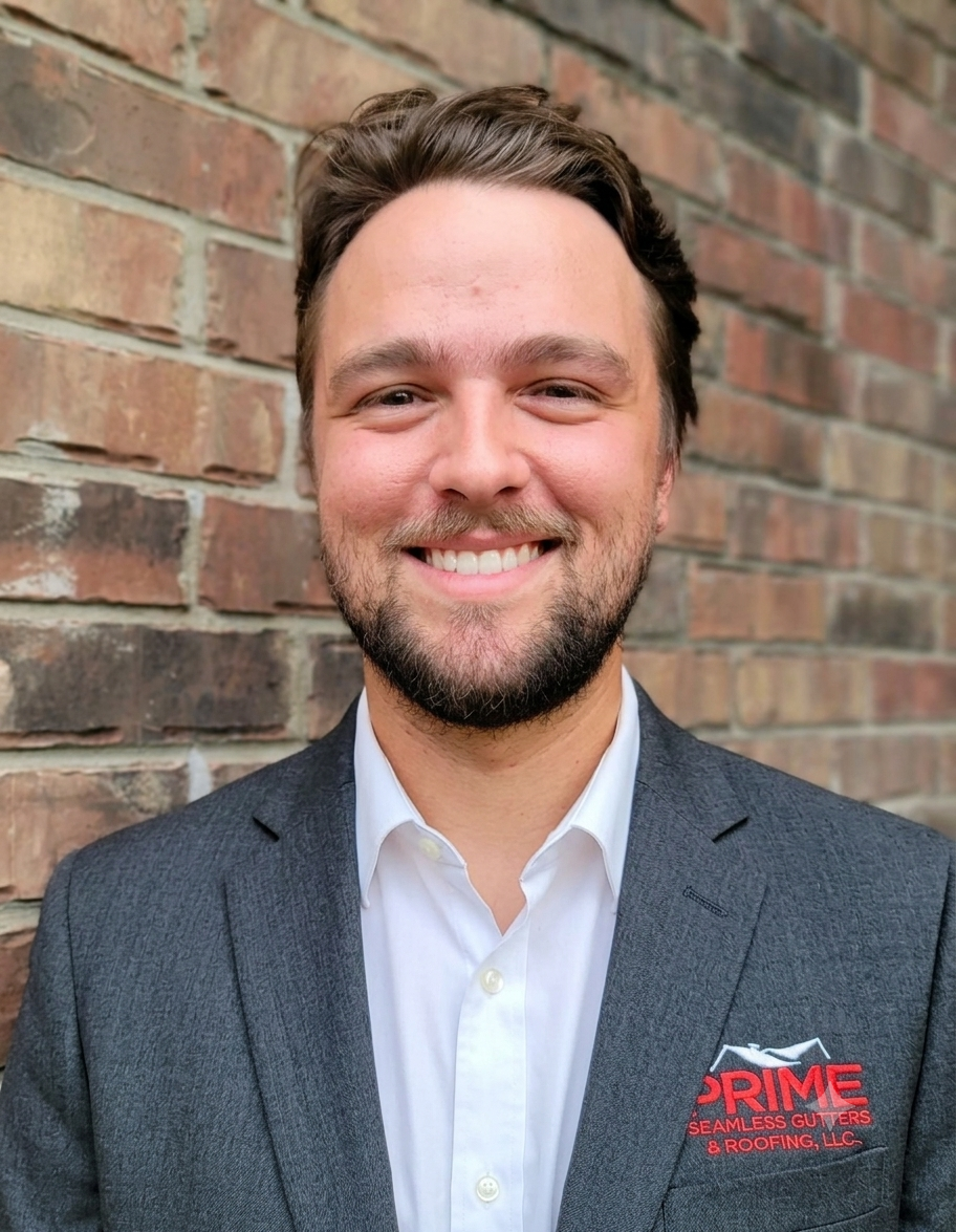 Professional headshot of Tim Doonan from Prime Seamless Gutters & Roofing, a San Antonio roofing and gutter company, wearing a gray blazer against a brick background