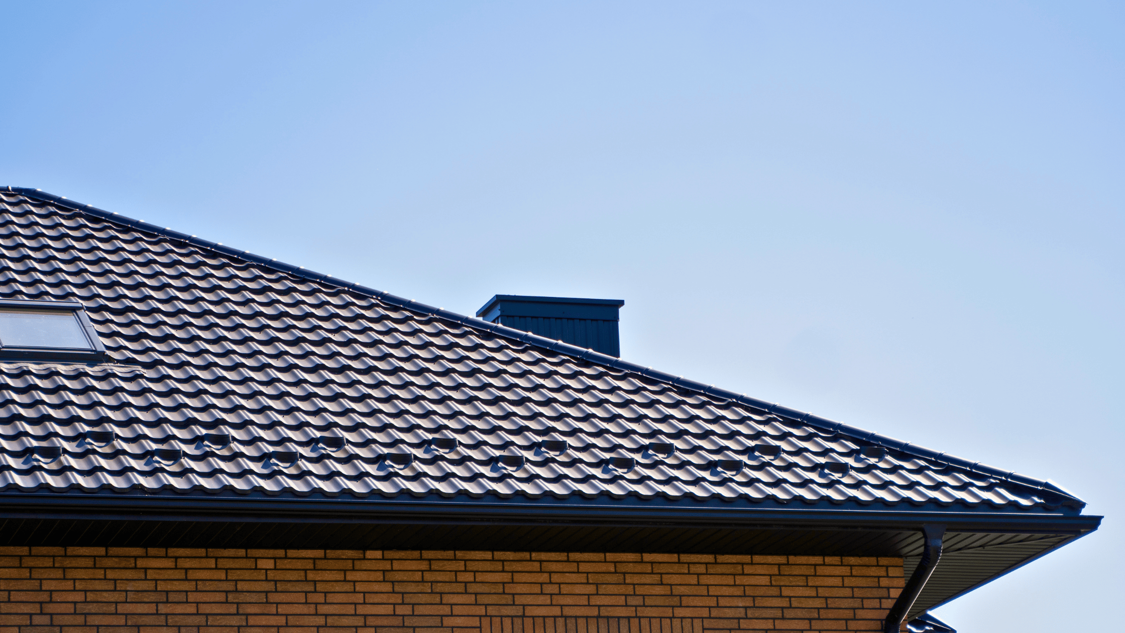 Modern dark tile roof with brick exterior wall and metal gutter, showcasing professional roofing and gutter installation work