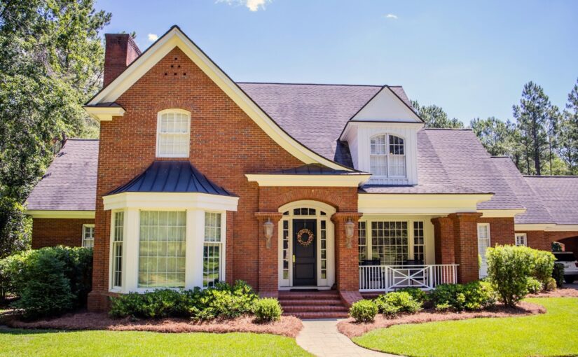 Brick colonial home with purple metal roof and white trim, featuring front porch and manicured landscaping